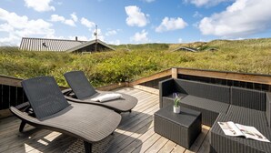 Une terrasse dotée de meubles en osier et d’un magazine, offrant une vue sur un paysage verdoyant avec des bâtiments visibles au loin.
