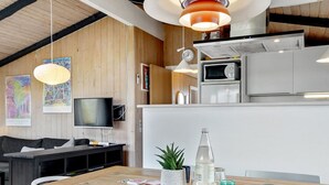 Une cuisine moderne avec des meubles blancs, un four à micro-ondes et une cuisinière. On y trouve une table à manger, une plante et une bouteille d’eau.