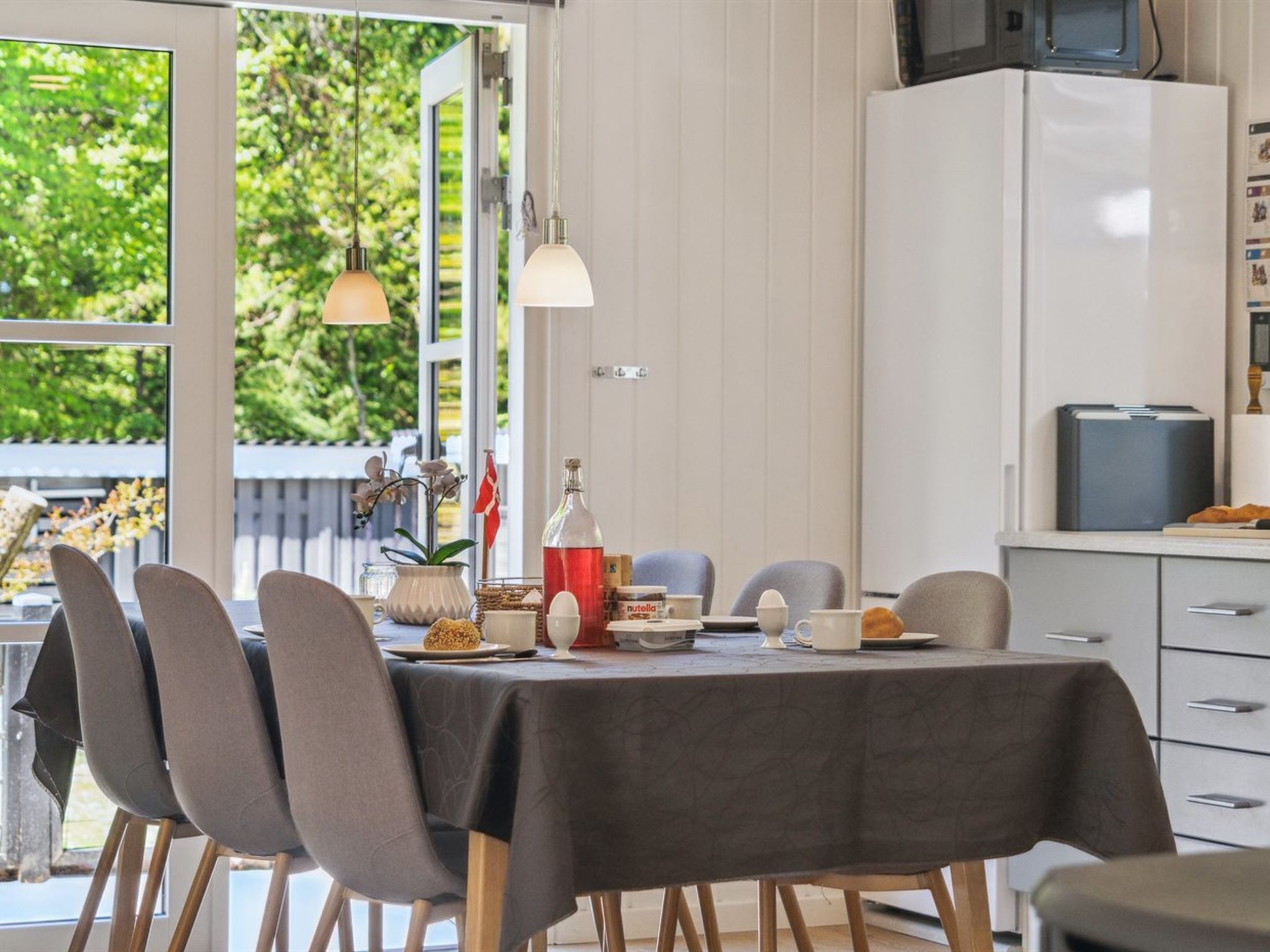 A dining area with a table set for four, chairs, a cabinet with a microwave, and a view of greenery outside.