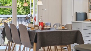 Comedor con mesa lista para cuatro personas, sillas, un mueble con microondas y vista a zonas verdes al exterior.