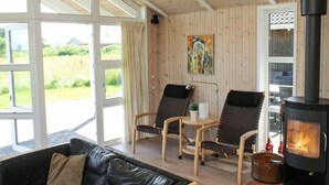 A cozy room with a black leather sofa, two armchairs, a small table, and a wood-burning stove. Large windows offer a view of the outdoors. - "Calina" - 300m from the sea by Interhome (Sæby)