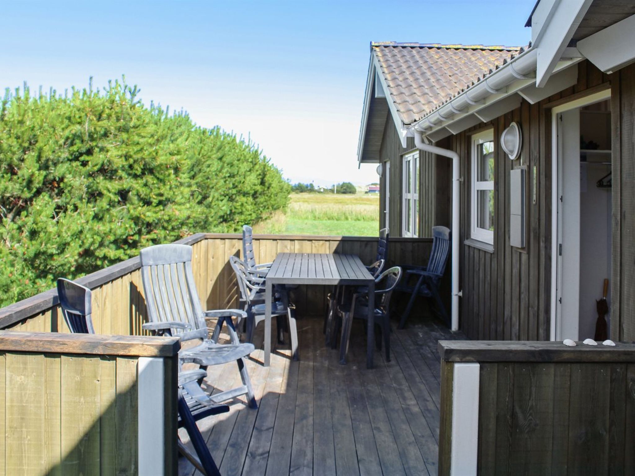Une terrasse en bois avec une table et des chaises, une clôture en bois et une maison avec un toit en tuiles.