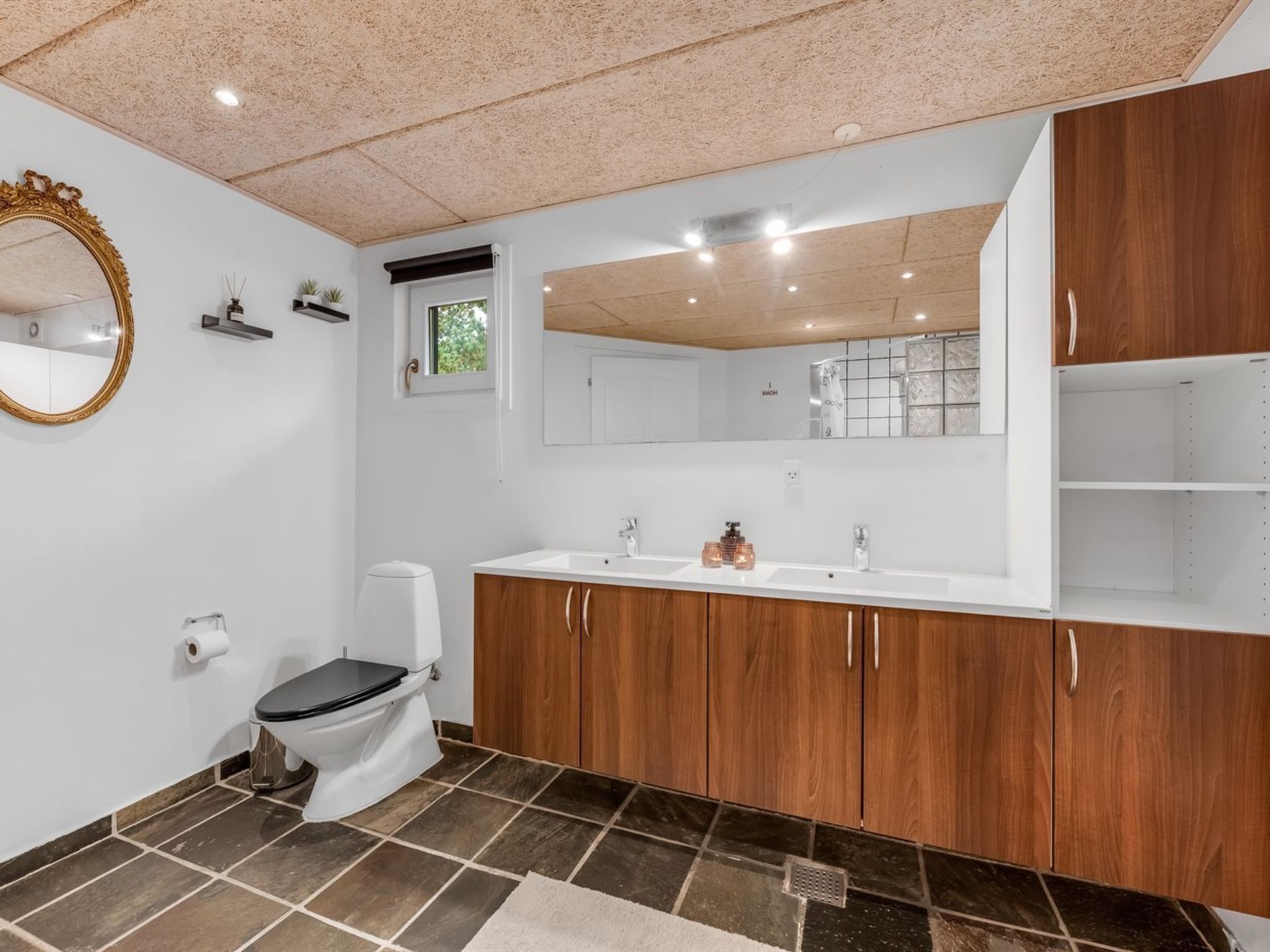 Een badkamer met toilet, wastafel, spiegel en houten kasten.