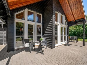 A wooden cabin with large windows and a patio area with outdoor furniture.