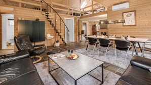 A spacious living area with a high ceiling, a staircase, a dining area, and a kitchen.