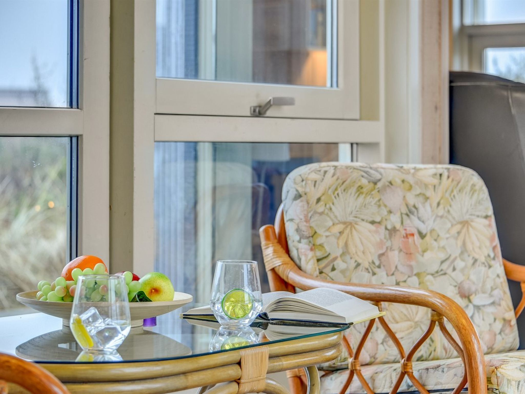 Een kamer met een glazen tafel, daarop fruit, een glas water en een boek.