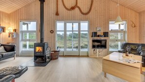Un intérieur de chalet chaleureux avec un poêle à bois, des meubles en cuir et de grandes fenêtres offrant une vue sur le paysage extérieur.