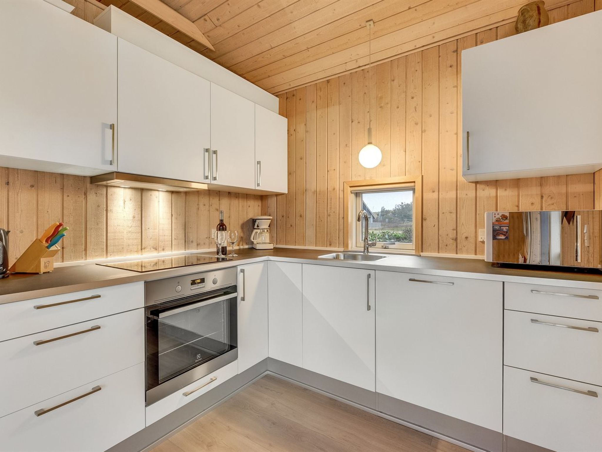 Eine moderne Küche mit weißen Schränken, einem eingebauten Backofen, einer Spüle und einem Fenster mit Blick ins Freie.