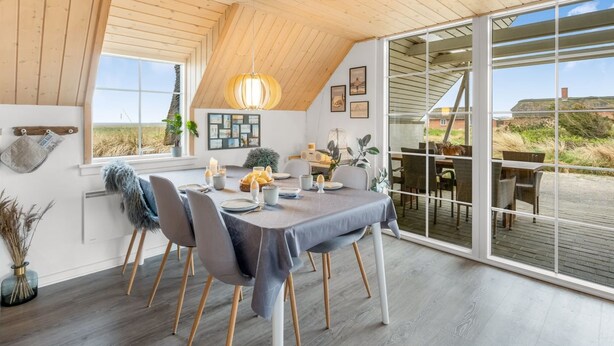 A dining area with a table set for four, wooden ceiling beams, and a large sliding glass door leading to an outdoor deck. - "Klimentina" - 150m from the sea by Interhome (Ringkøbing)