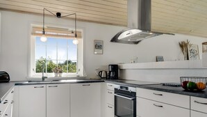 A modern kitchen with white cabinets, a built-in oven, and a window with a view of greenery.