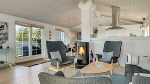 A spacious living room with a fireplace, two grey armchairs, a sofa, and a dining area with a table and chairs.