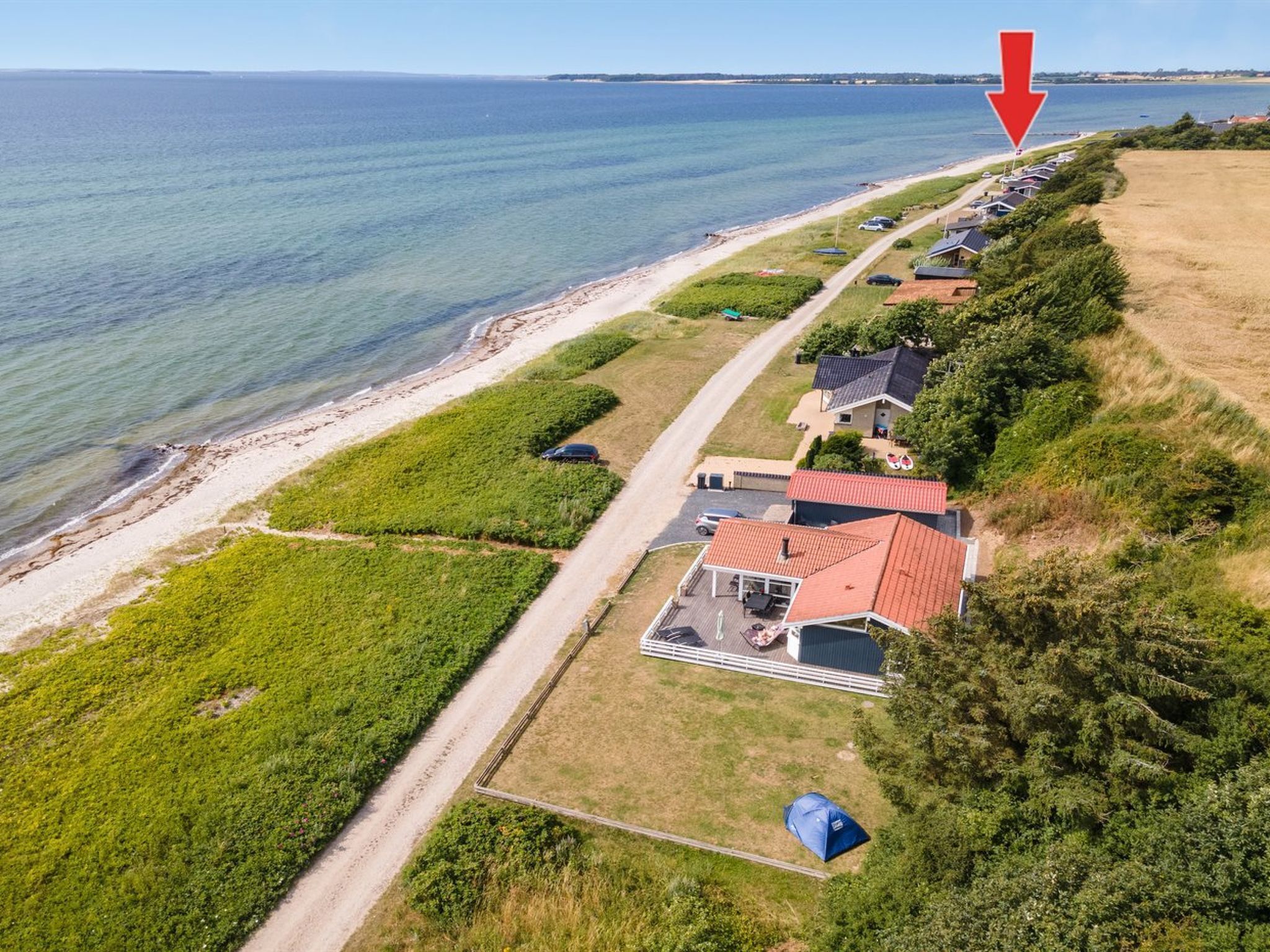 Vue aérienne d’une propriété située sur la côte, avec une rangée de maisons le long de la plage, un chemin dégagé menant à la plage et une tente installée sur la propriété.