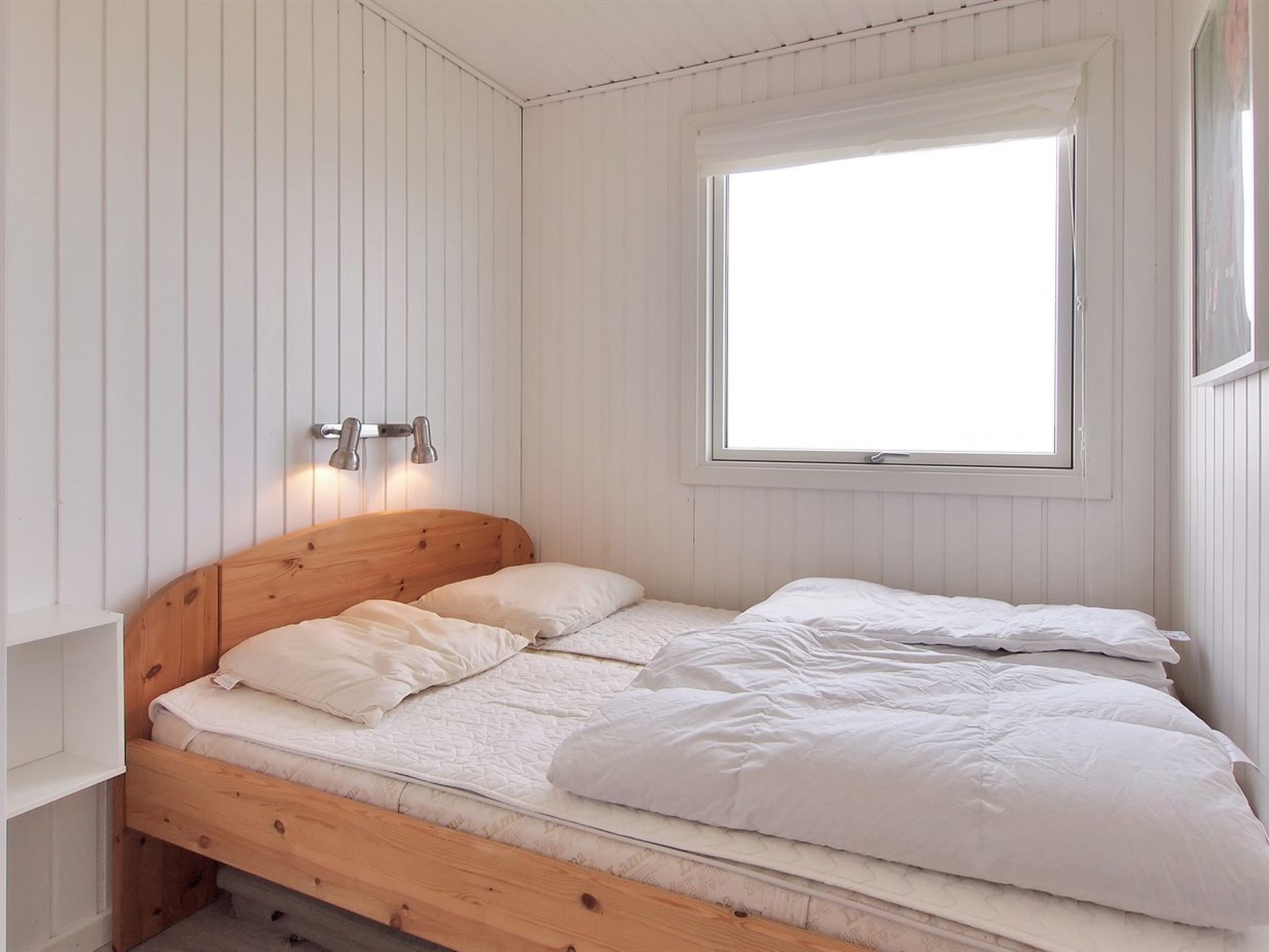 A single bed with a wooden headboard, white bedding, and a window with blinds.