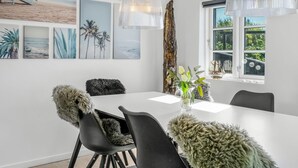 A modern dining area with a white table, black chairs, and a large window with a view of greenery. - "Wiebke" - 200m from the sea by Interhome (Blokhus)