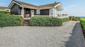 A modern house with a gravel driveway, a covered porch, and a view of the sea.