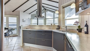 A modern kitchen with a large island, a view of the sea, and a dining area with chairs.