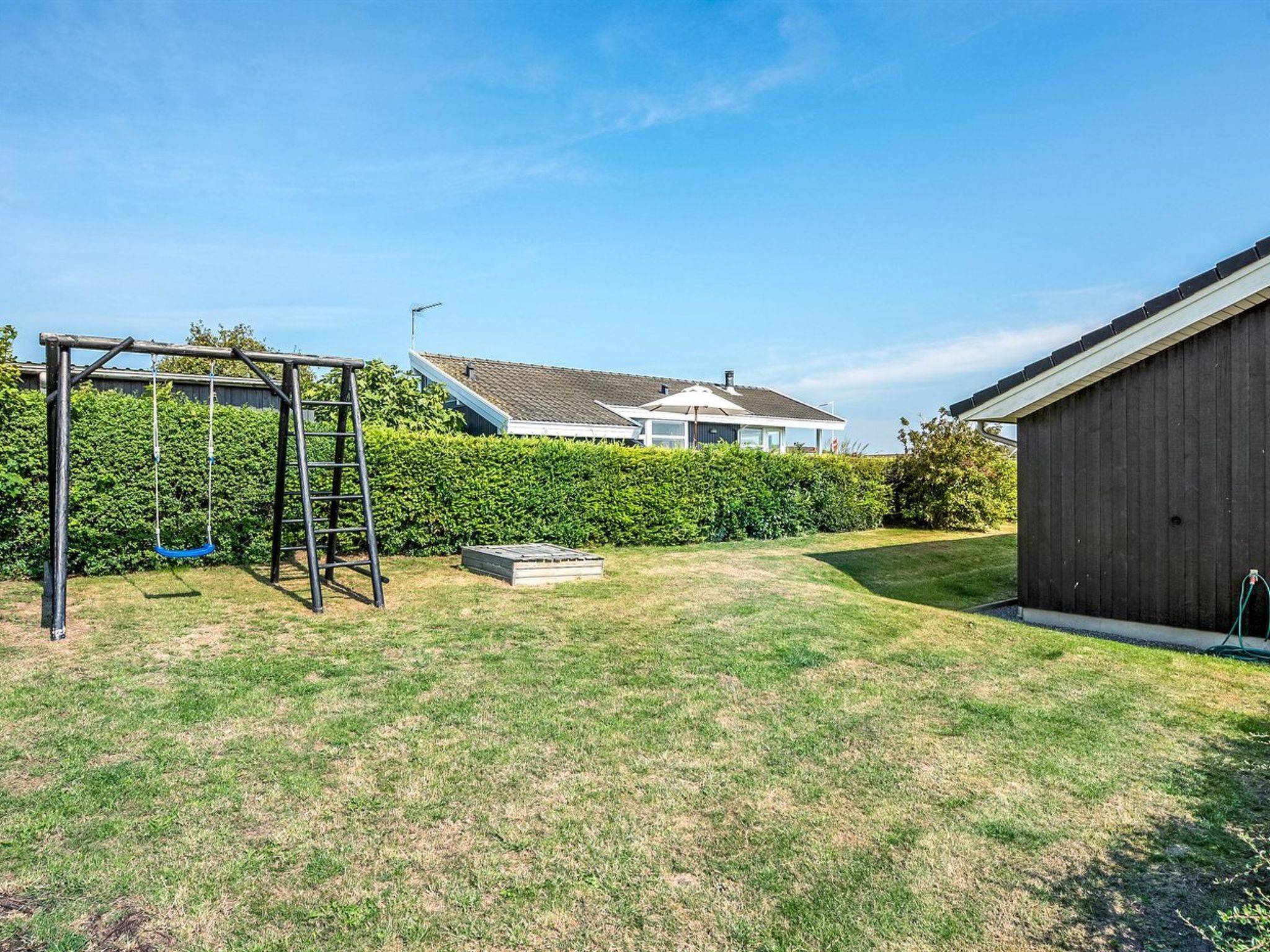 A backyard with a swing set, a wooden shed, and a well-maintained lawn.