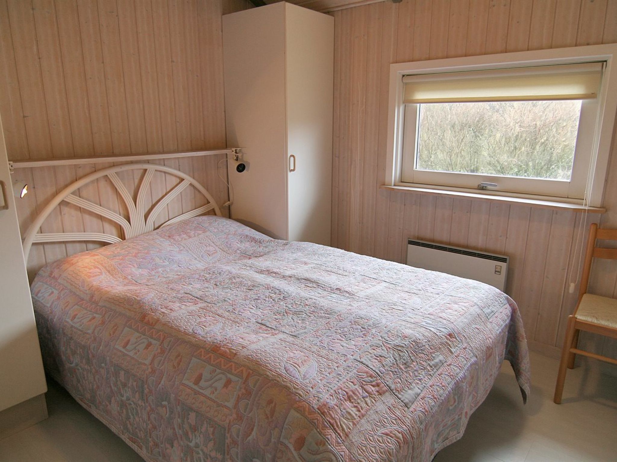 A bedroom with a bed, a wardrobe, a window, and a radiator.