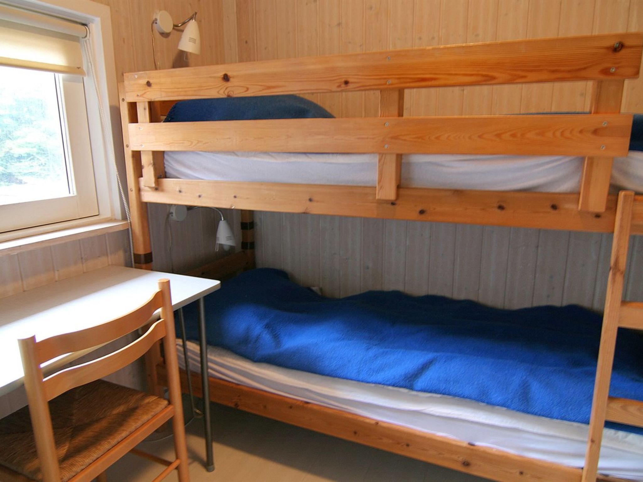 A bunk bed with a desk and chair, a lamp, and a window.