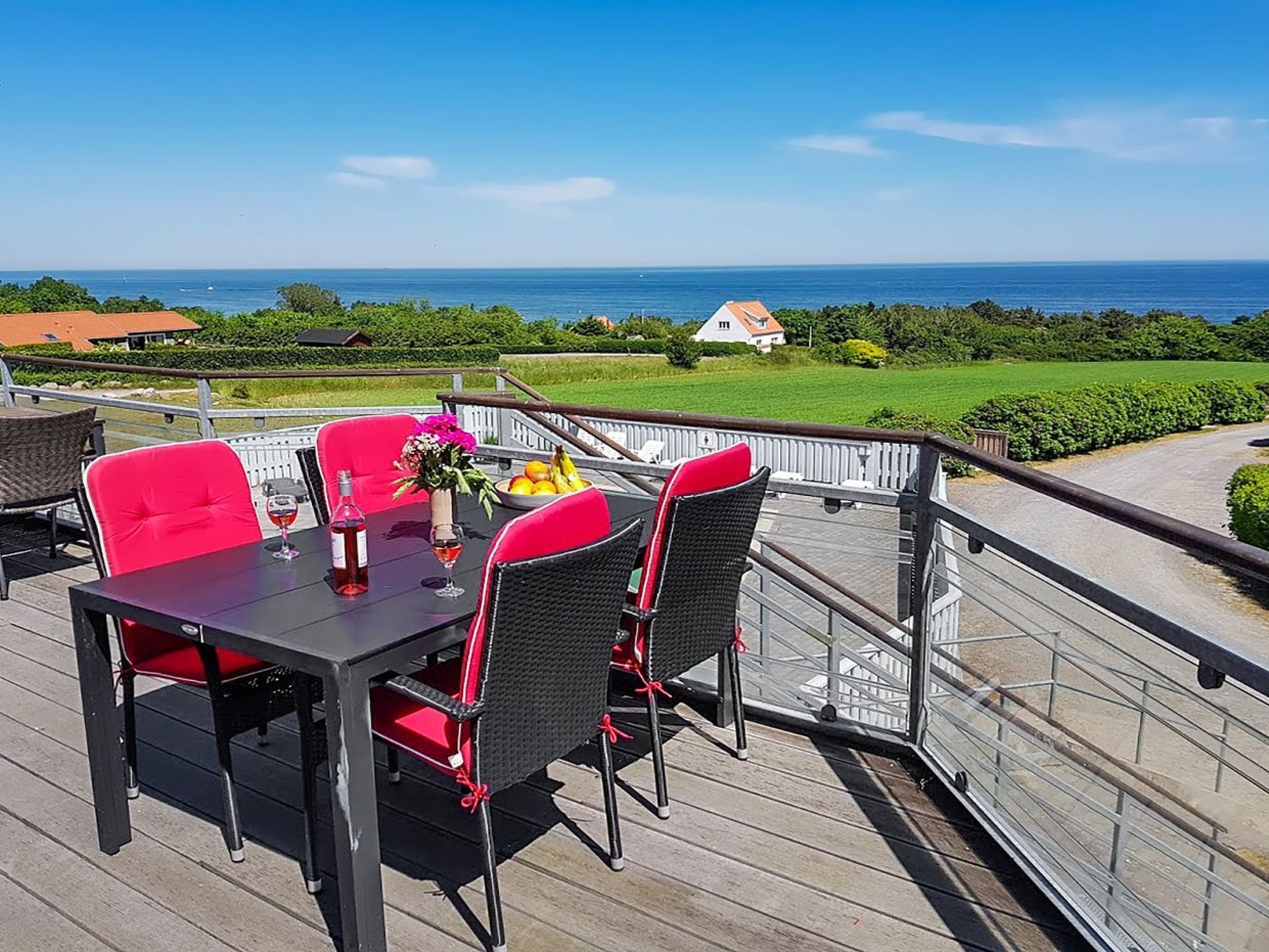A deck with a table and chairs, overlooking a coastal landscape with a house in the background.