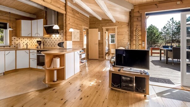 Ein modernes Blockhaus-Interieur mit Küche, Essbereich und Fernseher im Wohnzimmer.