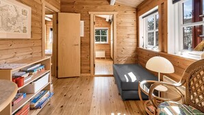 Ein gemütliches Blockhauss-Interieur mit Holzwänden, einer Bücherwand, einer Couch und einem Fenster mit Blick.