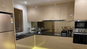 Una cocina moderna con armarios color beige, un refrigerador de acero inoxidable, un horno empotrado y una cafetera.