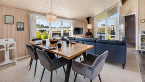 A modern living room with a wooden ceiling, a large window, a fireplace, and a dining area with a table and chairs.