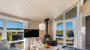 A modern living room with a fireplace, a flat-screen TV, and a large window overlooking a deck.