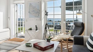 A spacious living room with a large window, a map on the wall, a table with a book, and a chair with a fur throw. - "Seba" - 500m from the sea by Interhome (Allinge)