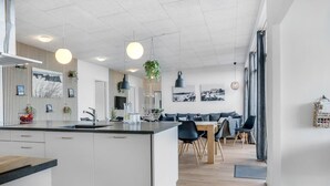 Et moderne køkken med en central ø, hvide skabe og et spiseområde med et træbord og stole.