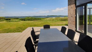 En terrasse med et bord og stole med udsigt over en græsplæne og vand.