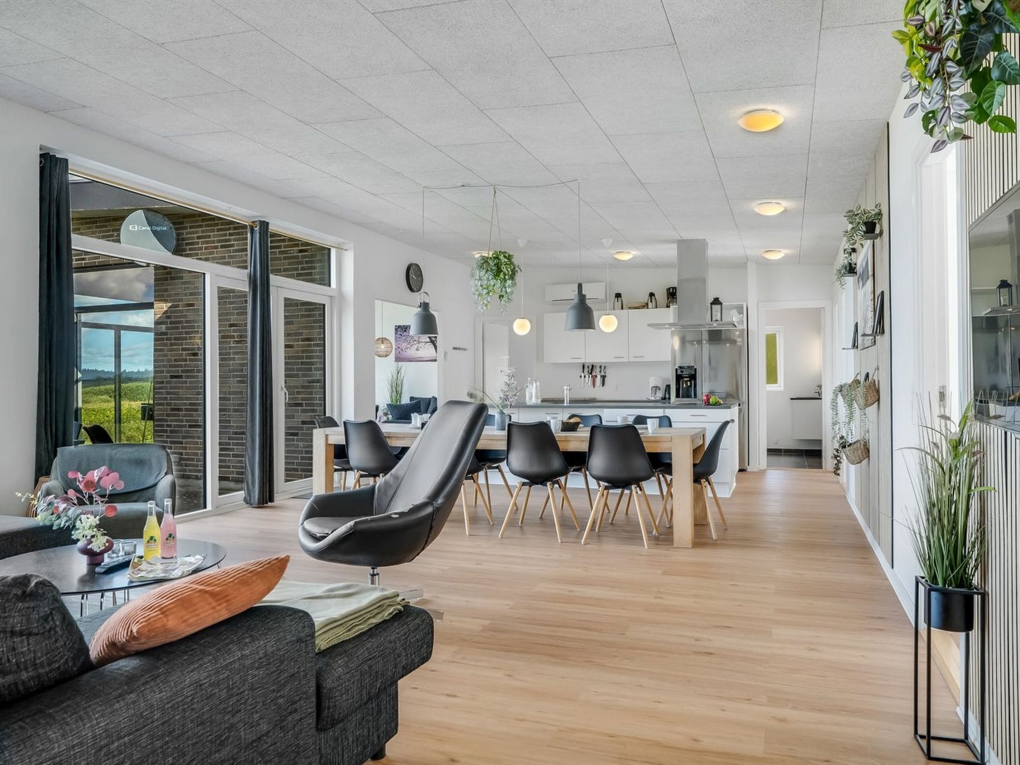 Una sala de estar moderna con un sofá, sillas y un comedor con mesa y sillas. Se observa una cocina al fondo, con armarios y electrodomésticos.