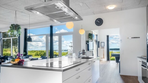 Et moderne køkken med en stor ø, et spiseområde med udsigt og en rummelig opholdsstue med et stort vindue der kigger ud over en sø.