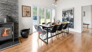 A modern dining area with a stone fireplace, a dining table with chairs, and a large window offering a view of the outdoors. - "Tenna" - 250m to the fjord by Interhome (Højslev)