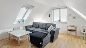 Een moderne loft slaapkamer met een schuine plafond, een grijze bank, een kleine tafel en een houten stoel.
