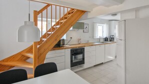 Een moderne keuken met witte kastjes, een houten trap en een eethoek met een witte tafel en stoelen.