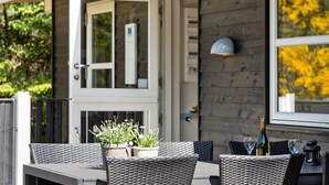 Un espace extérieur aménagé pour les repas, avec des meubles en osier, une table ornée d’une plante en pot et une bouteille de vin.