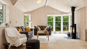 Un cuarto acogedor con paredes y techo de madera, una chimenea, dos sofás, una mesa y una ventana con vista a la vegetación.