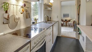 Cocina moderna con campana de acero inoxidable, pileta doble y una isla grande. Se observa un comedor con una silla de mimbre y una mesa.