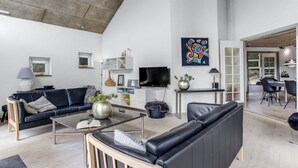 A spacious living room with a high ceiling, a large TV, and a dining area with a table and chairs.