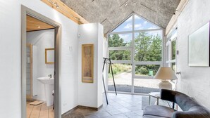 A modern interior with a stone ceiling, a large window offering a view of greenery, a black leather chair, and a white sink.