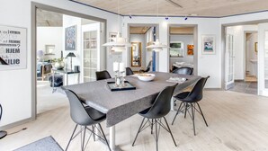 A modern dining area with a long table, black chairs, and pendant lighting.