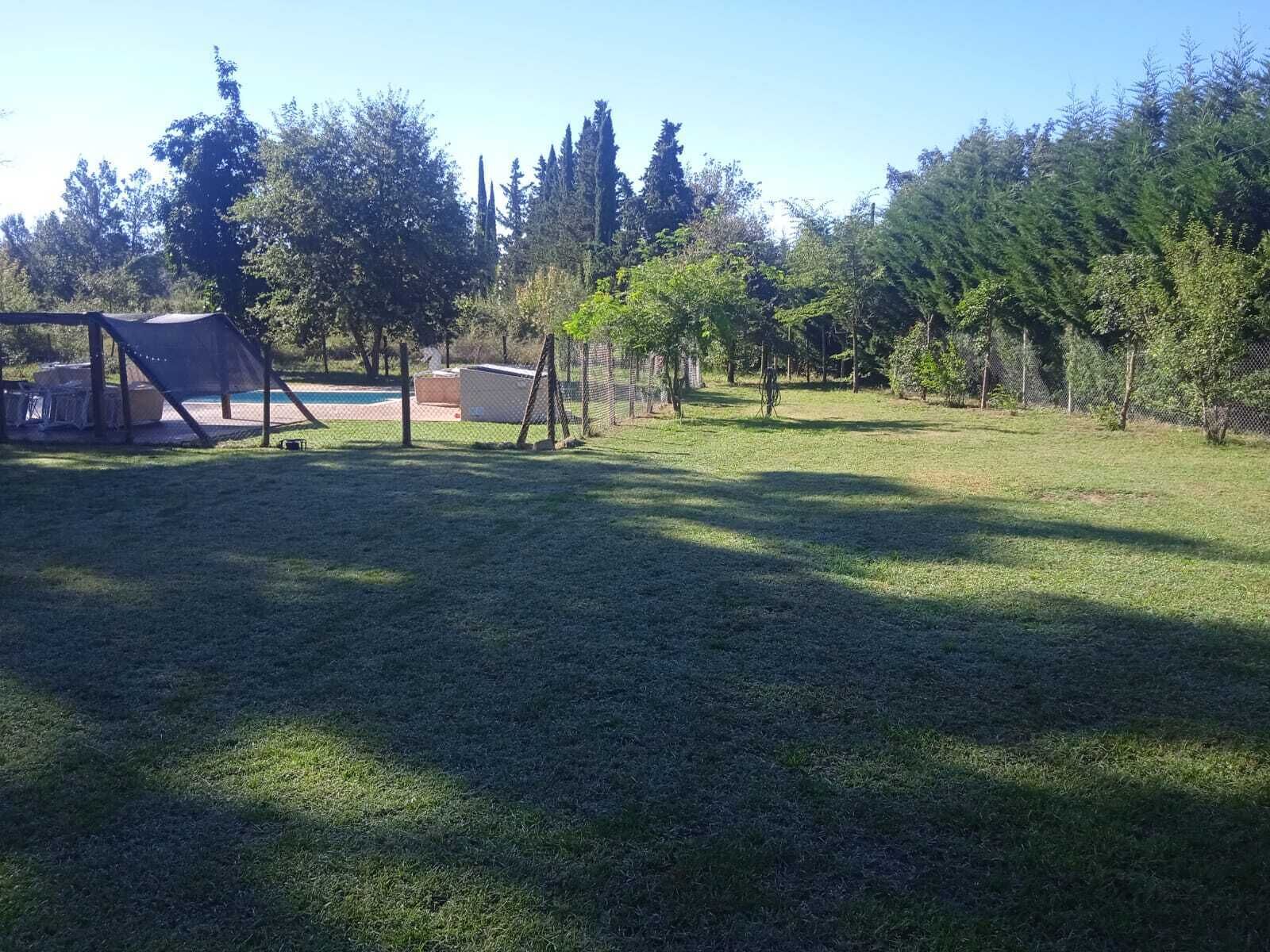 A grassy outdoor area with a swing set, a fenced play area, and trees.