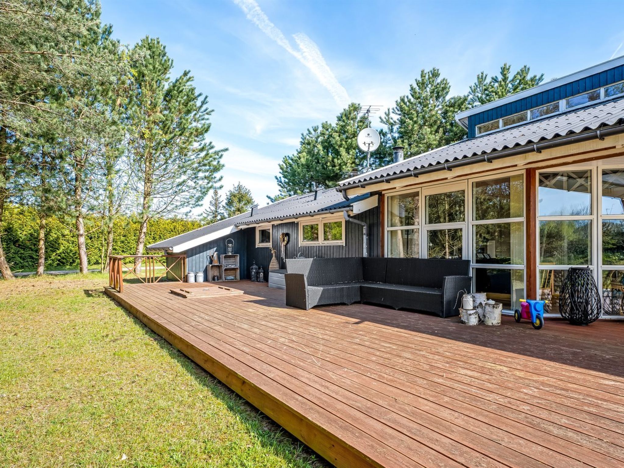 A modern cabin with a deck, large windows, and a satellite dish.