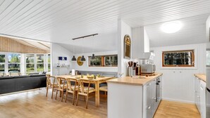 A modern kitchen with a wooden dining table, white cabinetry, and large windows.