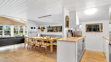 Une cuisine moderne avec une table à manger en bois, des meubles blancs et de grandes fenêtres.