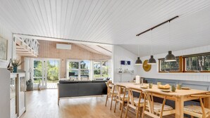 A spacious kitchen with wooden flooring, a dining area with a wooden table and chairs, and a view of the outdoors through large windows.