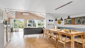 Une cuisine spacieuse avec un plancher en bois, un coin repas avec une table et des chaises en bois, et une vue sur l’extérieur grâce à de grandes fenêtres.
