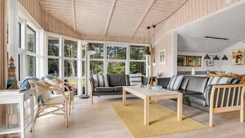 Un salon spacieux avec un plafond en bois, de grandes fenêtres, un canapé, une table basse et un coin repas.